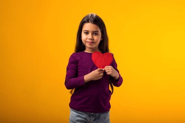 Portret van een meisje met een papieren hartje op een gele achtergrond. Liefde, zorg en Valentijnsdag concept - Foto, afbeelding