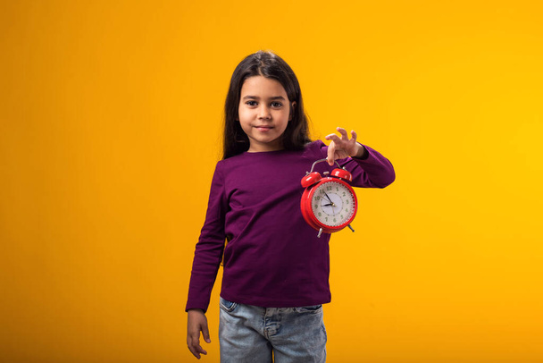 Mosolygó kislány portréja, amint egy ébresztőórát tart a kezében. Az oktatás fogalma, az iskola, a határidők, a tanulás ideje - Fotó, kép