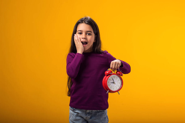 Портрет удивленной девочки с будильником в руке. Понятие образования, школа, сроки, время на учебу - Фото, изображение