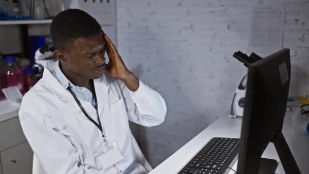 Afrikanischer Wissenschaftler im Laborkittel, der in einem Labor mit Computer und Geräten Kopfschmerzen ausdrückt - Filmmaterial, Video