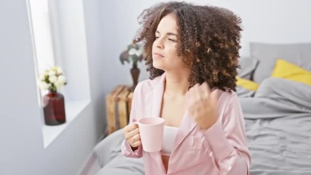 Modern yatak odası ortamında kahvesini yudumlayan kıvırcık saçlı genç İspanyol kadın, rahat bir sabahı canlandırıyor.. - Video, Çekim