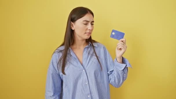Злий молодий іспаномовний жінка відкидає жест великими пальцями вниз, показуючи нелюбов, оскільки вона тримає кредитну картку на ізольованому жовтому тлі - Кадри, відео