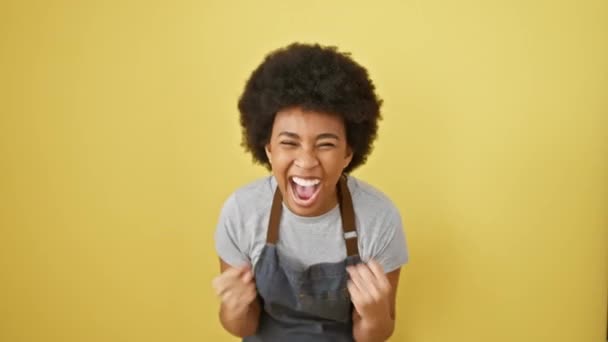 Joyeuse femme afro-américaine en tablier célèbre la victoire, criant d'excitation et de bonheur tout en faisant geste gagnant sur fond jaune isolé - Séquence, vidéo