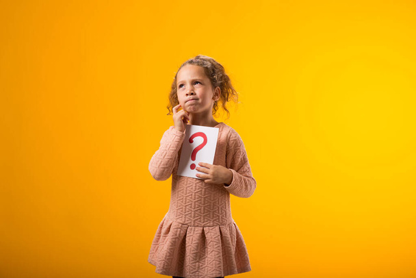 Ein Porträt eines nachdenklichen Mädchens mit Fragezeichen. Kinder, Idee und Wissenskonzept - Foto, Bild
