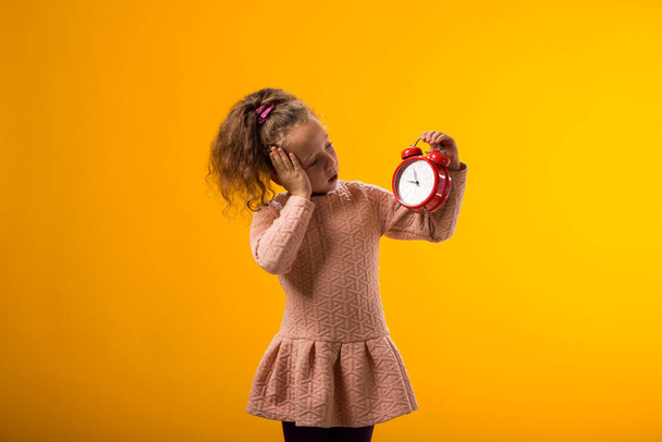 Egy meglepett kislány portréja, amint egy ébresztőórát tart a kezében. Az oktatás fogalma, az iskola, a határidők, a tanulás ideje - Fotó, kép