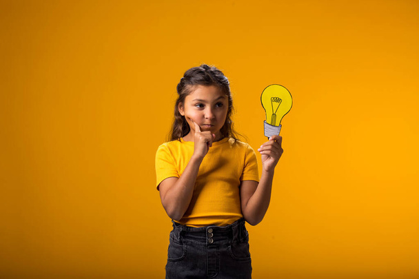 Portrét přemýšlivé holčičky držící papírovou žárovku. Úspěch, motivace, vítěz, génius, idea koncept - Fotografie, Obrázek