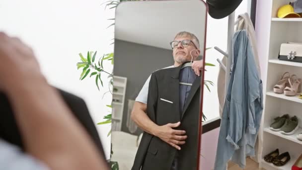 volwassen man in bril probeert op een pak vest in een moderne kleedkamer, reflecteren op stijl keuzes. - Video