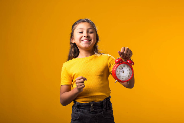 Портрет улыбающейся девочки с будильником в руке. Понятие образования, школа, сроки, время на учебу - Фото, изображение