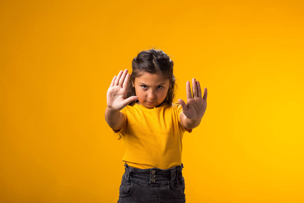 Retrato de niña mostrando gesto de stop sobre fondo amarillo. Concepto de bulling y emociones negativas - Foto, Imagen