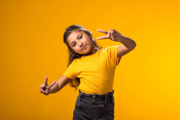 Mosolygó kislány portréja, ahogy a kamerát nézi sárga háttér felett. Gyermekkor és pozitív érzelmek fogalma - Fotó, kép