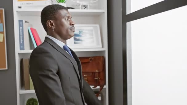 Itsevarma mies puvussa seisoo huomaavaisesti modernissa toimistossa, johon sisältyy ammattimaisuus ja keskittyminen.. - Materiaali, video