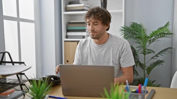 Um empresário casual com barba trabalha de um escritório em casa, usando um laptop e atender chamadas em um ambiente moderno e interno. - Filmagem, Vídeo