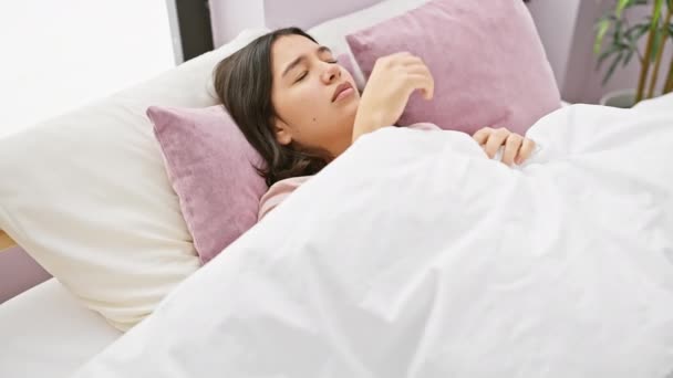 Μια νεαρή Ισπανίδα ξαπλωμένη στο κρεβάτι με πονοκέφαλο, σε ένα άνετο εσωτερικό υπνοδωμάτιο, απεικονίζοντας ασθένεια ή δυσφορία. - Πλάνα, βίντεο
