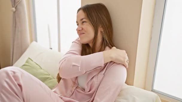 Egy rózsaszín pizsamás fiatal nő pihen a napfényes hálószobájában, testesíti meg a kényelmet és a szabadidőt a házban.. - Felvétel, videó