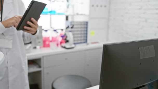 Luotettava naistutkija käyttää tablettia nykyaikaisessa laboratoriossa, jota ympäröivät laitteet ja ruskeat pullot.. - Materiaali, video