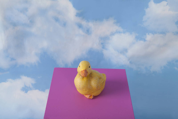a plaster duck on a pink cube in front of a blue sky with clouds.Minimal still life photography - Photo, Image