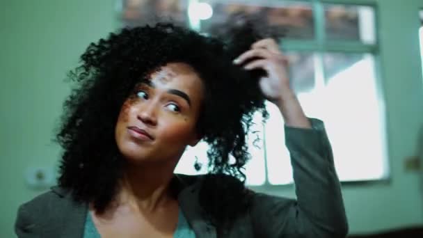 Uma jovem mulher latina negra brinca com o cabelo encaracolado na frente do espelho se preparando para sair. Irritado afro-americano adulto menina em 20s não gostando de seu próprio olhar - Filmagem, Vídeo