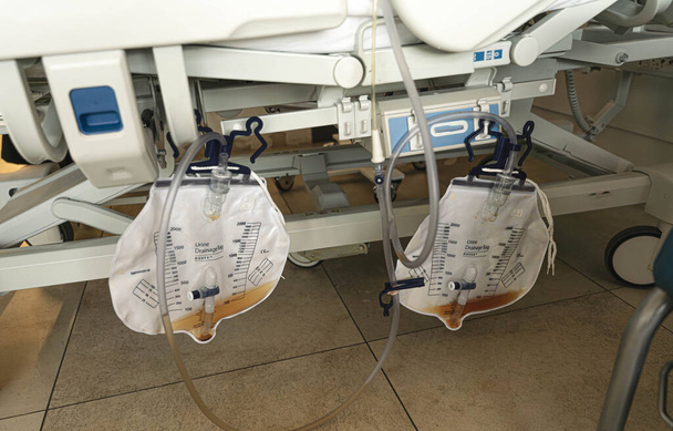 Spodní část nemocničního lůžka ukazuje dva pytle moči odebrané trubicemi a katetry - Fotografie, Obrázek