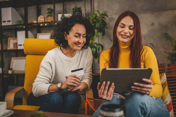 két nő yound felnőtt és érett nők használja hitelkártya otthon vásárlás online keresés interneten keresztül digitális tabletta a foglalás valós emberek másolás hely - Fotó, kép