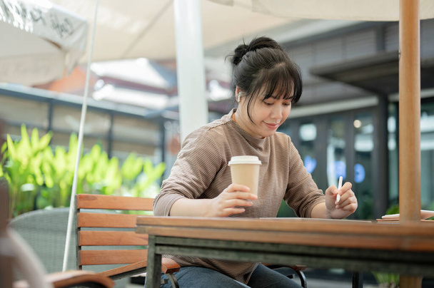Una bella e concentrata donna asiatica sta lavorando a distanza in un caffè della città, usando il suo tablet digitale. freelance, studente, donna d'affari, nomade digitale - Foto, immagini