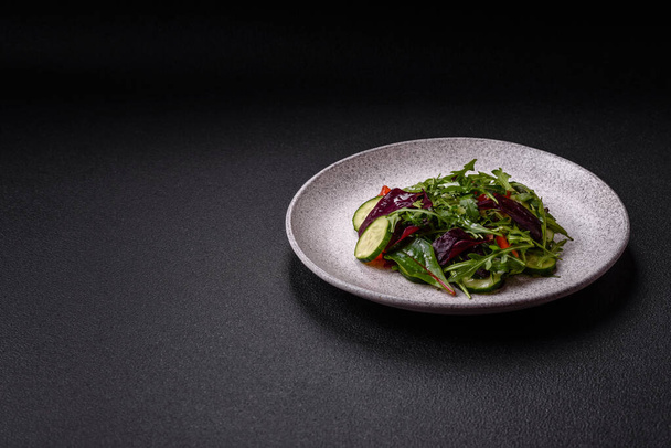 Πεντανόστιμη φρέσκια σαλάτα με ρόκα, σπανάκι, αγγούρι και ντοματίνια σε κεραμικό πιάτο σε σκούρο μπετόν φόντο - Φωτογραφία, εικόνα