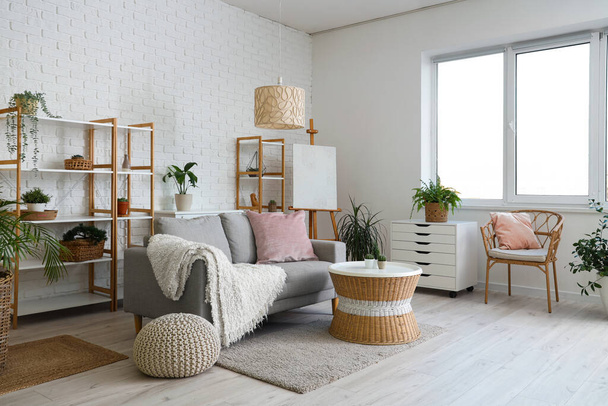 Loft stijl interieur van lichte woonkamer met gezellige bank, lade, tafel, kamerplanten, planken, fauteuil en ezel - Foto, afbeelding