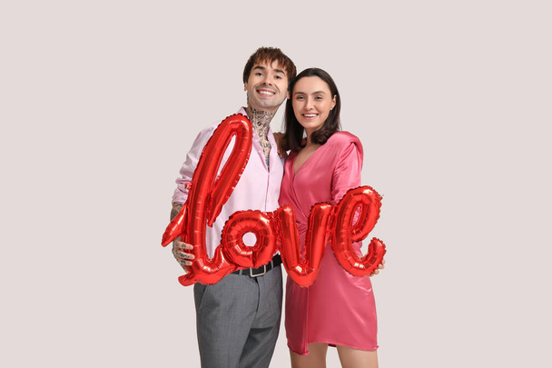 白い背景に愛という言葉の形をした気球を持つ若いカップル. バレンタインデーのお祝い - 写真・画像