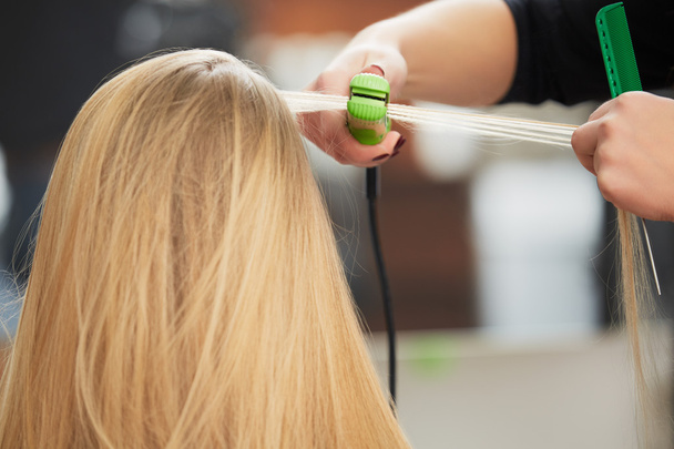 Hairdresser curling hair with straightener - Фото, изображение