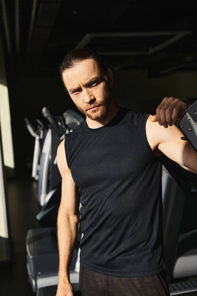 Ein athletischer Mann in aktiver Kleidung steht selbstbewusst neben einer Reihe von Laufbändern in einem Fitnessstudio, bereit für sein Workout. - Foto, Bild