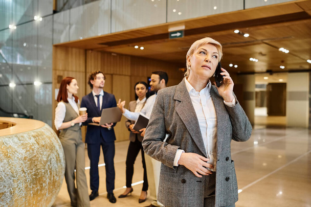 Una mujer se dirige con confianza a un grupo de negocios interracial usando su teléfono celular. - Foto, imagen