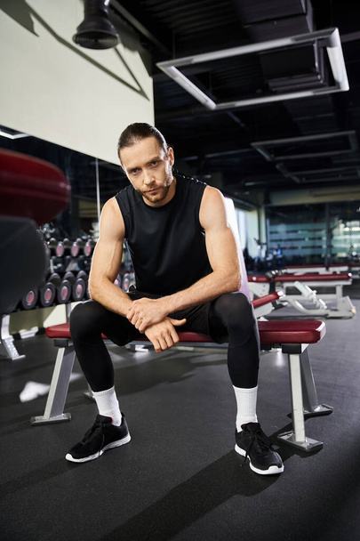 Ein athletischer Mann in Trainingsausrüstung sitzt auf einer Gymnastikbank und macht eine Pause von seinem energischen Trainingsalltag. - Foto, Bild