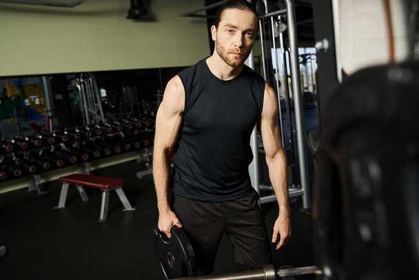 Um homem musculoso vestido em activewear fica em um ginásio, segurando uma placa preta. - Foto, Imagem