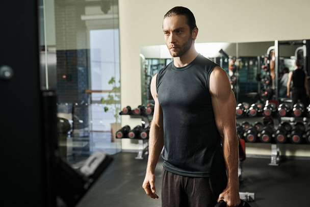 Mężczyzna w sportowym stroju stoi na siłowni, trzymając czarne talerze. - Zdjęcie, obraz