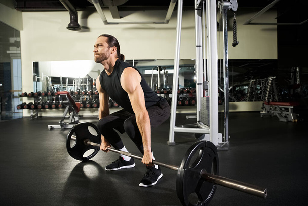Een gefocuste man in actieve kleding voert een squat uit met een lange halter in een sportschool, toont kracht en vastberadenheid. - Foto, afbeelding