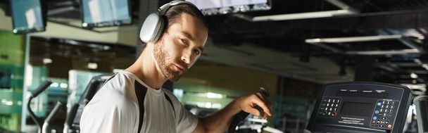 Un homme athlétique en tenue active utilise une machine tout en portant un casque pour une séance d'entraînement musicale améliorée. - Photo, image