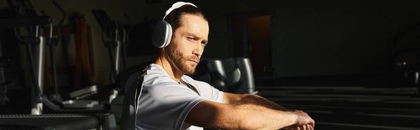 Een gefocuste man in actieve kleding zit in een sportschool en luistert naar muziek via een koptelefoon.. - Foto, afbeelding