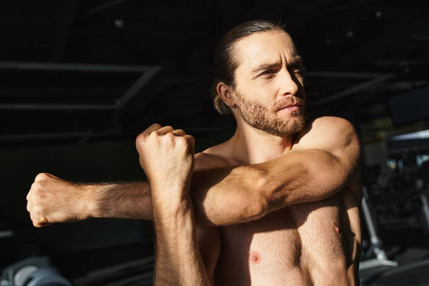 Hombre sin camisa mostrando físico muscular, flexionando bíceps en un ambiente de gimnasio con confianza y determinación. - Foto, imagen