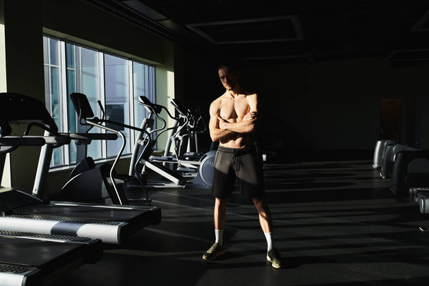 Ein muskulöser Mann ohne Hemd steht selbstbewusst vor einer Reihe von Laufbändern in einer Turnhalle. - Foto, Bild