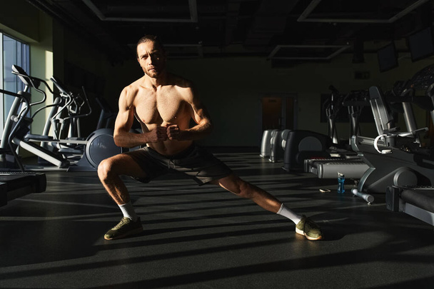 muskularny mężczyzna bez koszuli robi squat ćwiczenia w siłowni z determinacją i skupieniem. - Zdjęcie, obraz