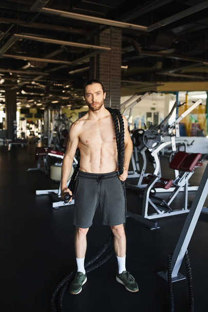 Un uomo muscoloso senza camicia, in piedi in palestra, che mostra la sua dedizione al fitness e al training di forza. - Foto, immagini