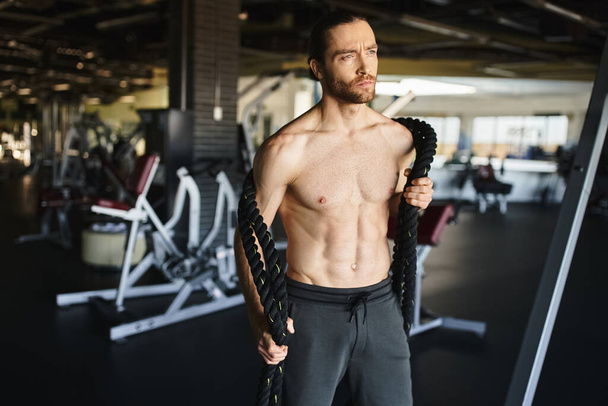 Bezkoszulkowy, muskularny mężczyzna intensywnie skupiony na treningu siłowym z ciężkimi linami. - Zdjęcie, obraz