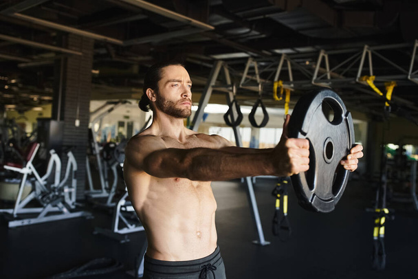 Mężczyzna bez koszulki pewnie podnosi sztangę na siłowni, pokazując swoją muskularną sylwetkę i poświęcenie dla fitness. - Zdjęcie, obraz