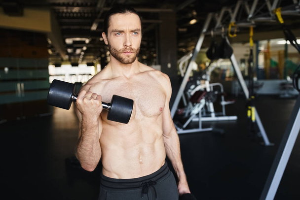 Un hombre sin camisa mostrando su inmensa fuerza, sosteniendo dos pesas, en la intensa atmósfera de un gimnasio. - Foto, imagen