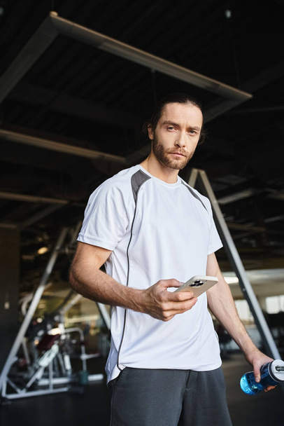 Un hombre con una camisa blanca involucrado en su teléfono inteligente después del entrenamiento en el gimnasio - Foto, Imagen