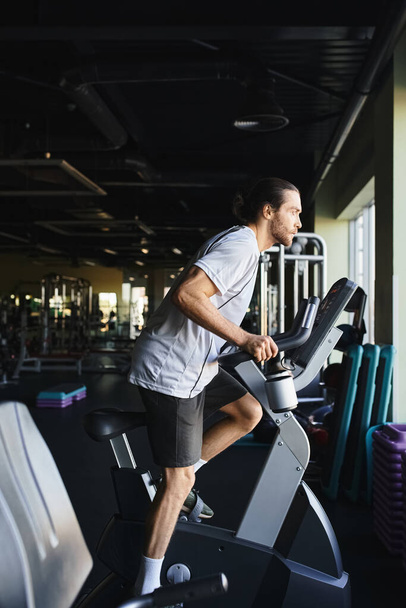 Muskulöser Mann, der an seine Grenzen stößt, sprintet auf einem stationären Fahrrad in einem modernen Fitnessstudio-Umfeld. - Foto, Bild