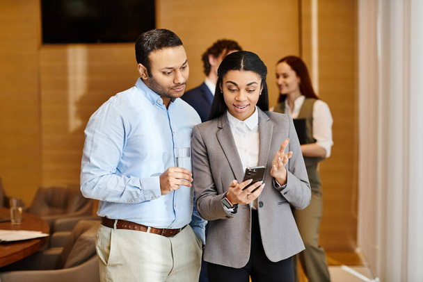 Un hombre y una mujer de un grupo interracial de gente de negocios están absortos en mirar un teléfono celular juntos. - Foto, Imagen