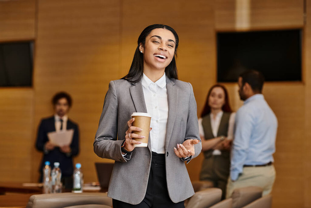 Una mujer de color disfrutando de una taza de café en una sala de reuniones de negocios diversa. - Foto, Imagen