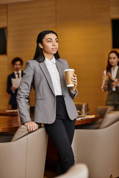 Una donna afroamericana in giacca e cravatta con una tazza di caffè. - Foto, immagini