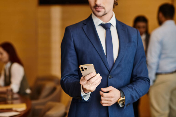 Un uomo d'affari diversificato in giacca e cravatta tiene con fiducia un cellulare. - Foto, immagini