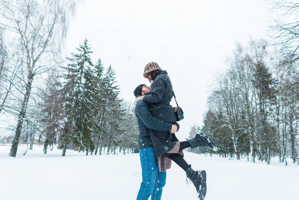 ファッショナブルで美しい幸せな恋人のファッション冬の服は雪と冬の公園で楽しんでいます. ハンサムな男は彼のガールフレンドの女性を拾った - 写真・画像